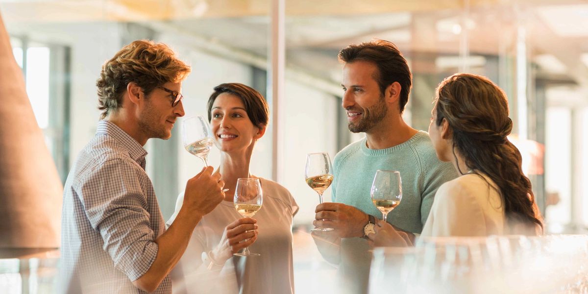 A group of smiling people standing and sipping from wine glasses, enjoying a bottle of white wine together.