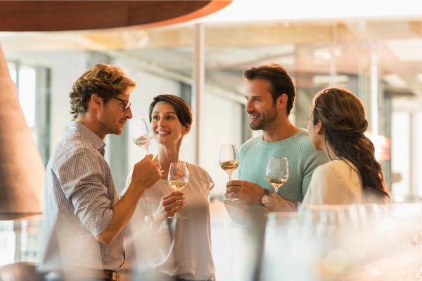 A group of smiling people standing and sipping from wine glasses, enjoying a bottle of white wine together.