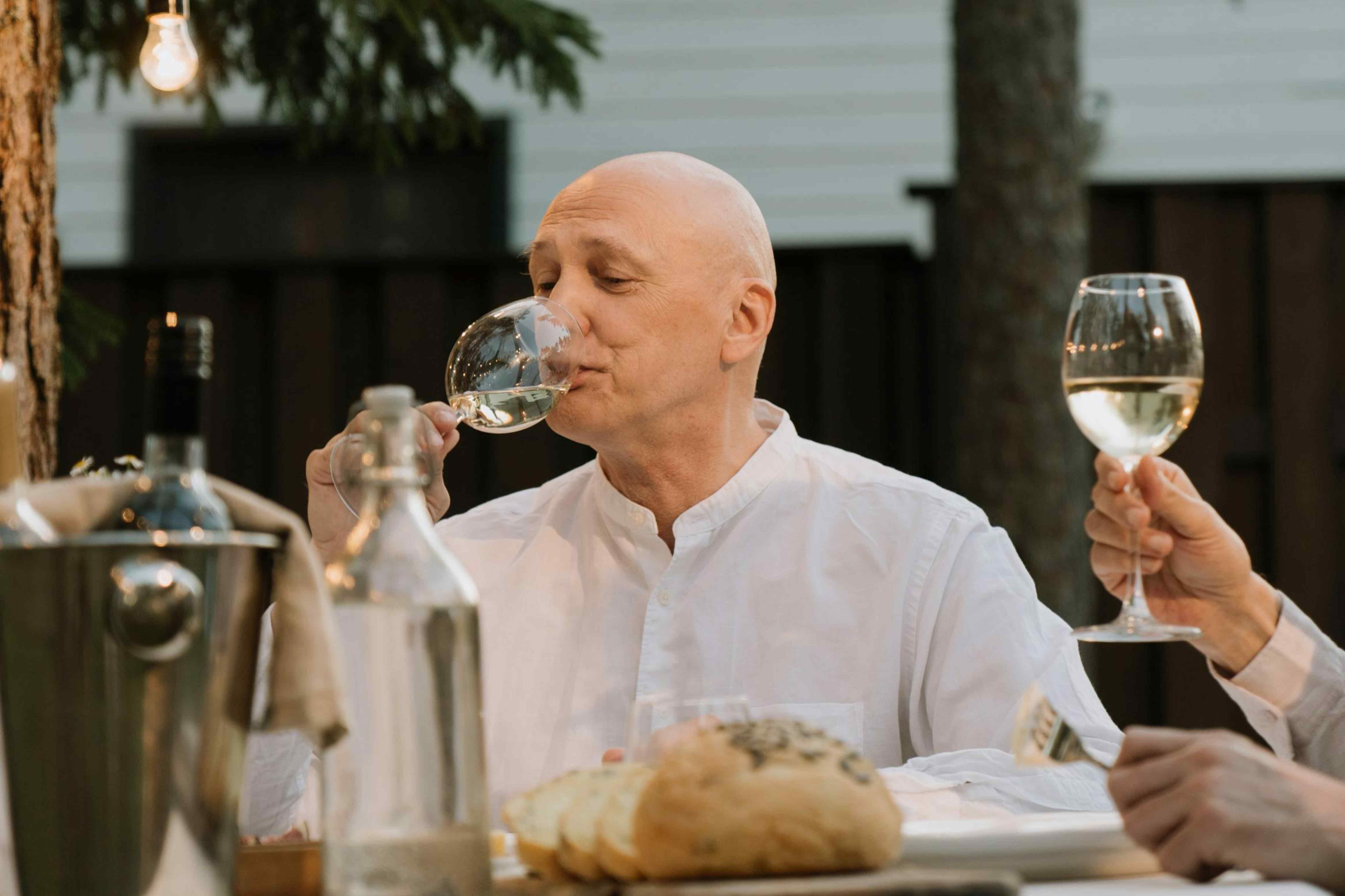 A man enjoying a glass of white wine at an outdoor dinner table.