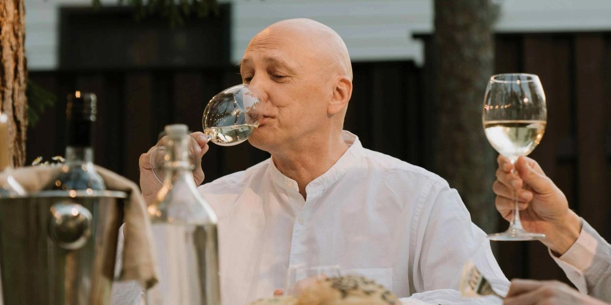 A man enjoying a glass of white wine at an outdoor dinner table.