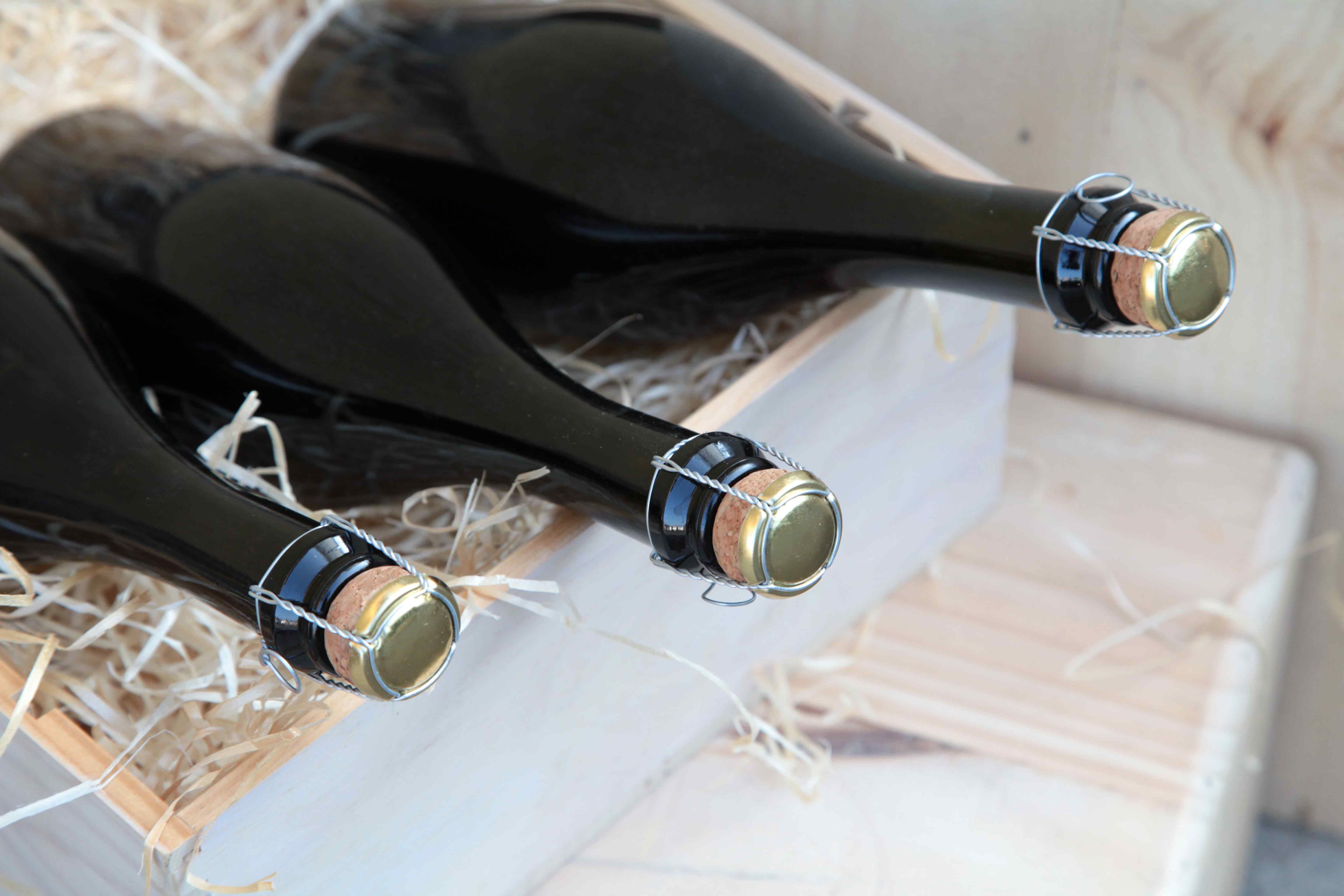 Wine bottles with wire cage tops packed horizontally in a wooden crate with straw packing material.