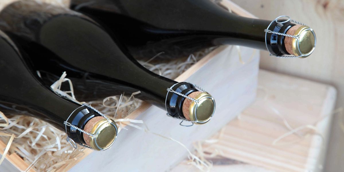 Wine bottles with wire cage tops packed horizontally in a wooden crate with straw packing material.