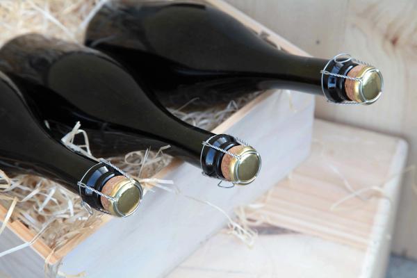 Wine bottles with wire cage tops packed horizontally in a wooden crate with straw packing material.