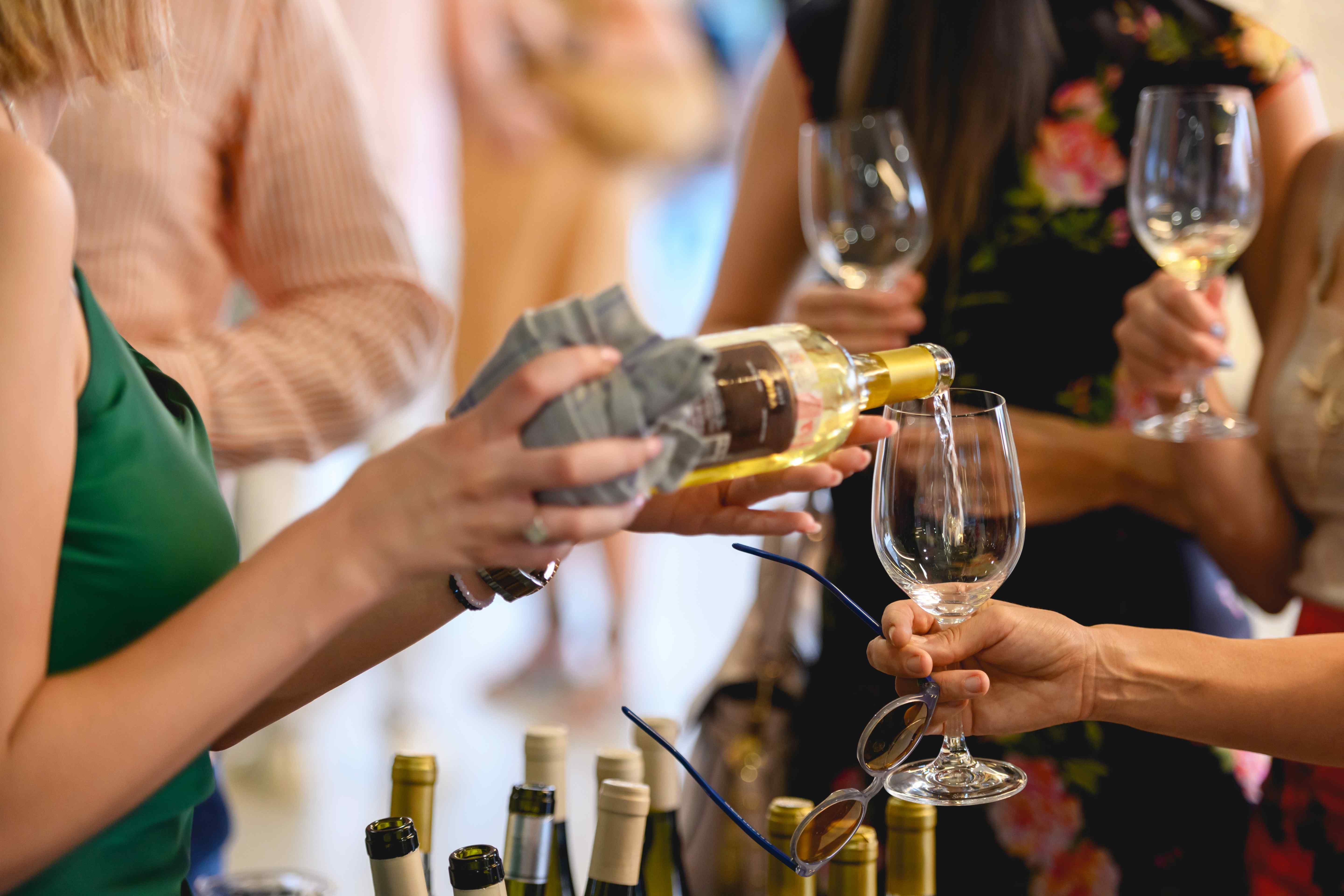 A group of people at a wine tasting with white wine being poured into a glass.