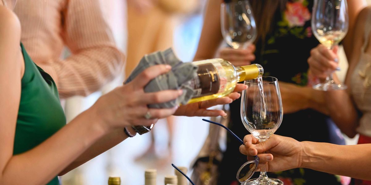 A group of people at a wine tasting with white wine being poured into a glass.