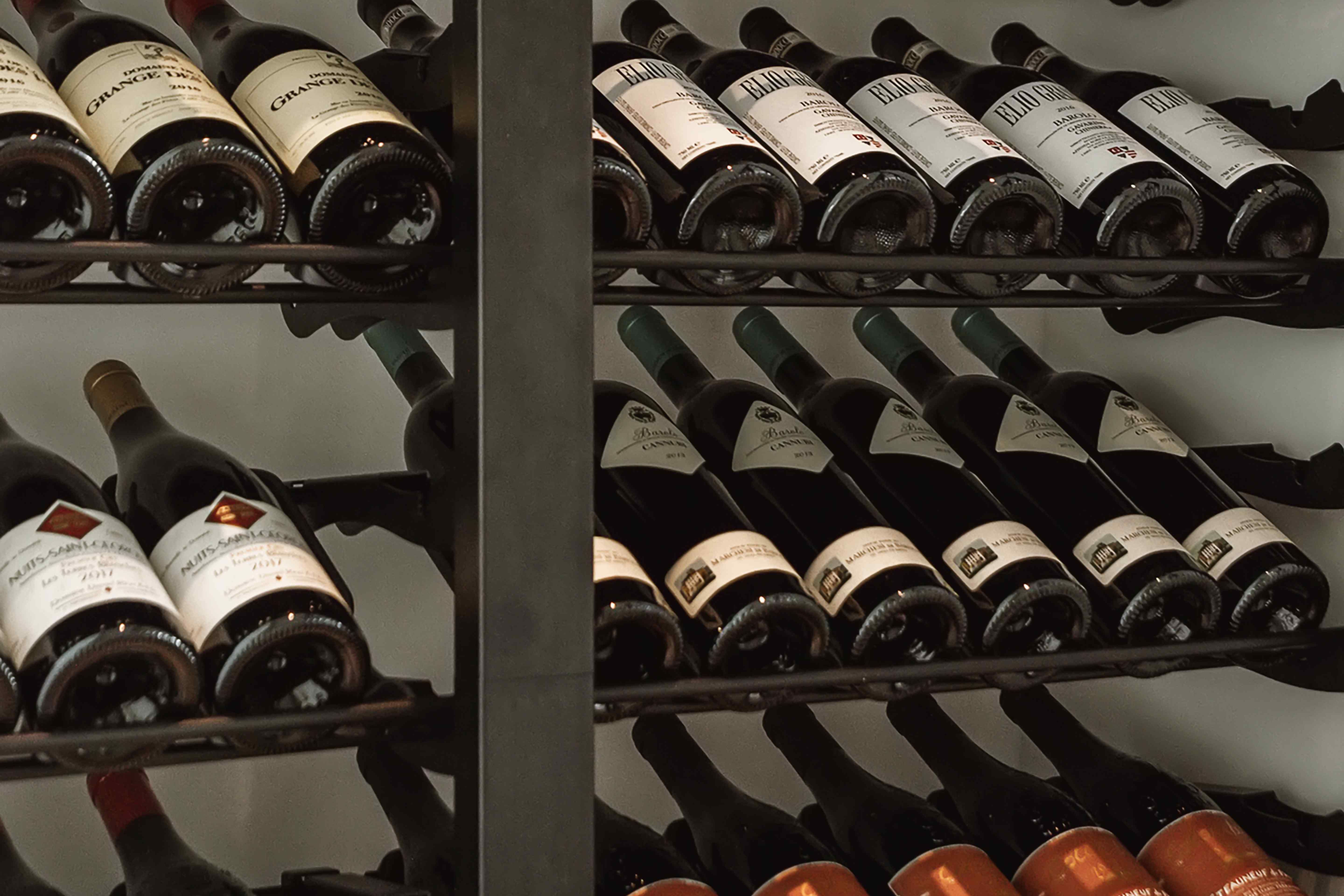 Wine bottles stored label-forward on metal cellar racks in a restaurant, including Barolo and Burgundy vintages.