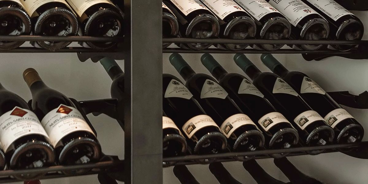 Wine bottles stored label-forward on metal cellar racks in a restaurant, including Barolo and Burgundy vintages.