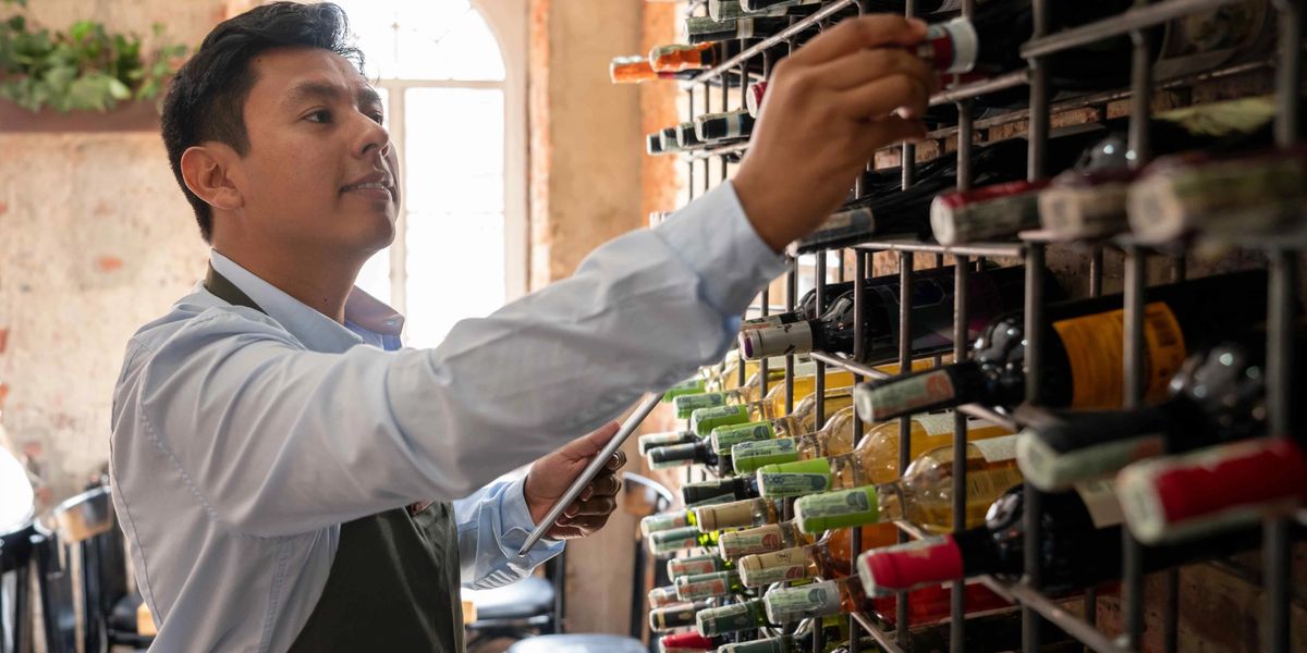 Collector referencing a digital wine inventory while selecting a bottle from a large cellar rack.