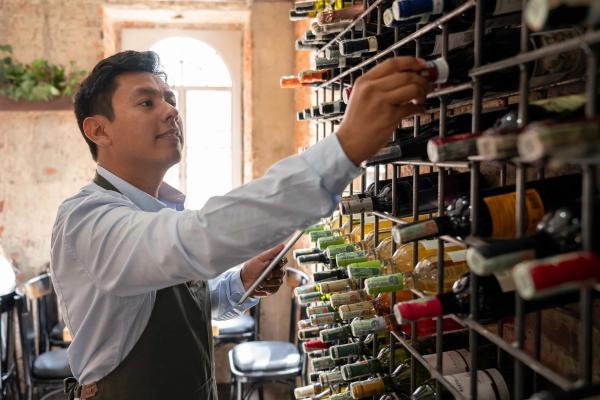 Collector referencing a digital wine inventory while selecting a bottle from a large cellar rack.