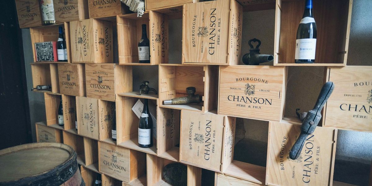 A wall of stacked wooden Burgundy wine cases used as shelving, holding bottles, antique cellar taps and an oak barrel.