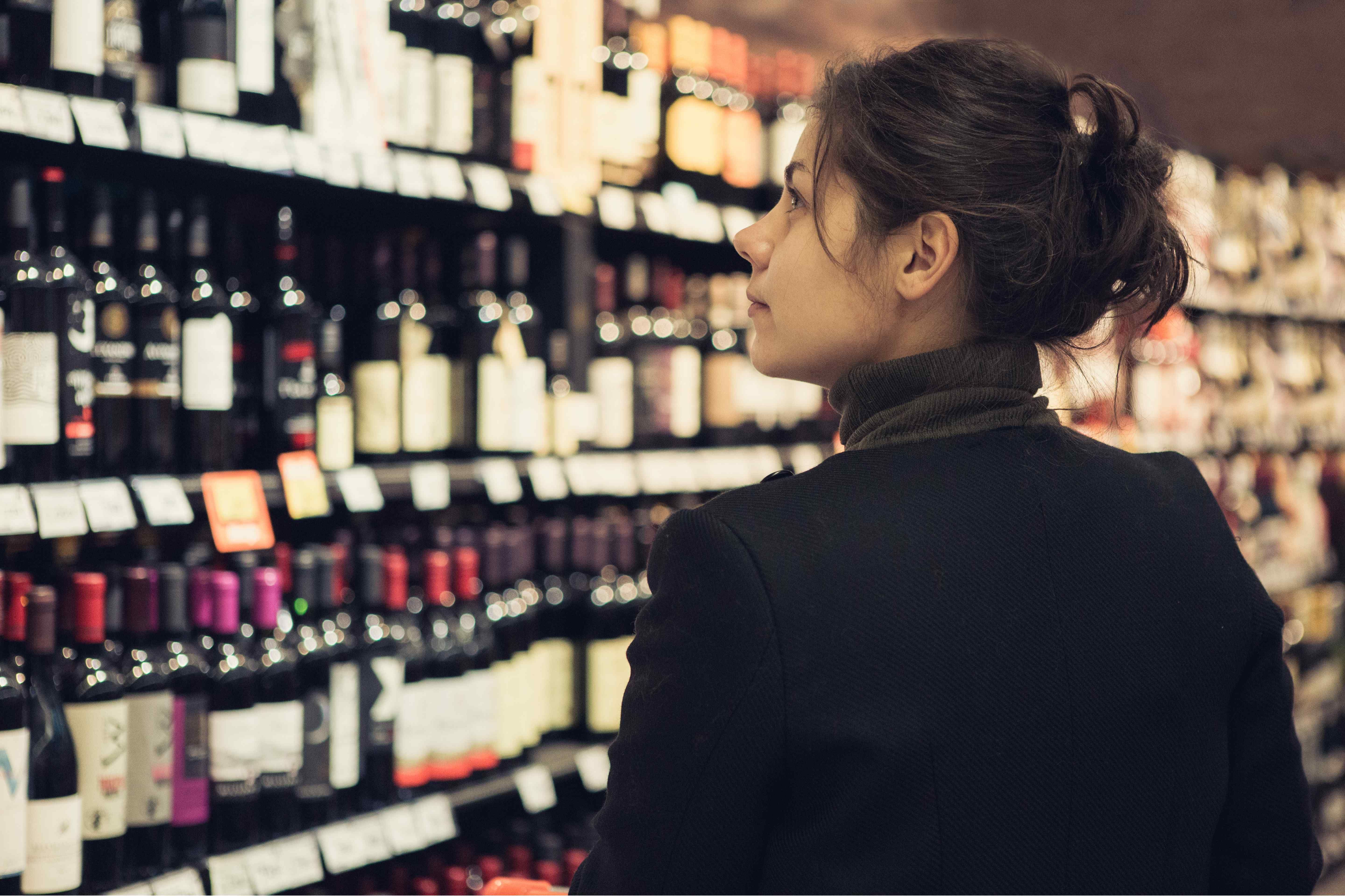 Woman browsing rows of wine bottles on shelves in a wine shop.