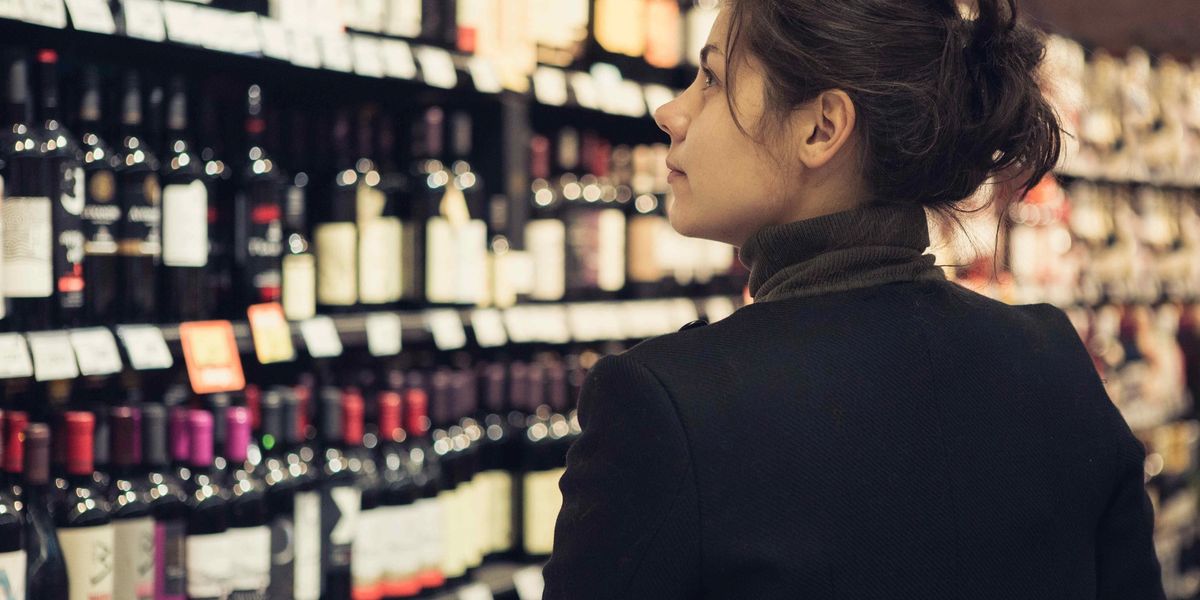 Woman browsing rows of wine bottles on shelves in a wine shop.