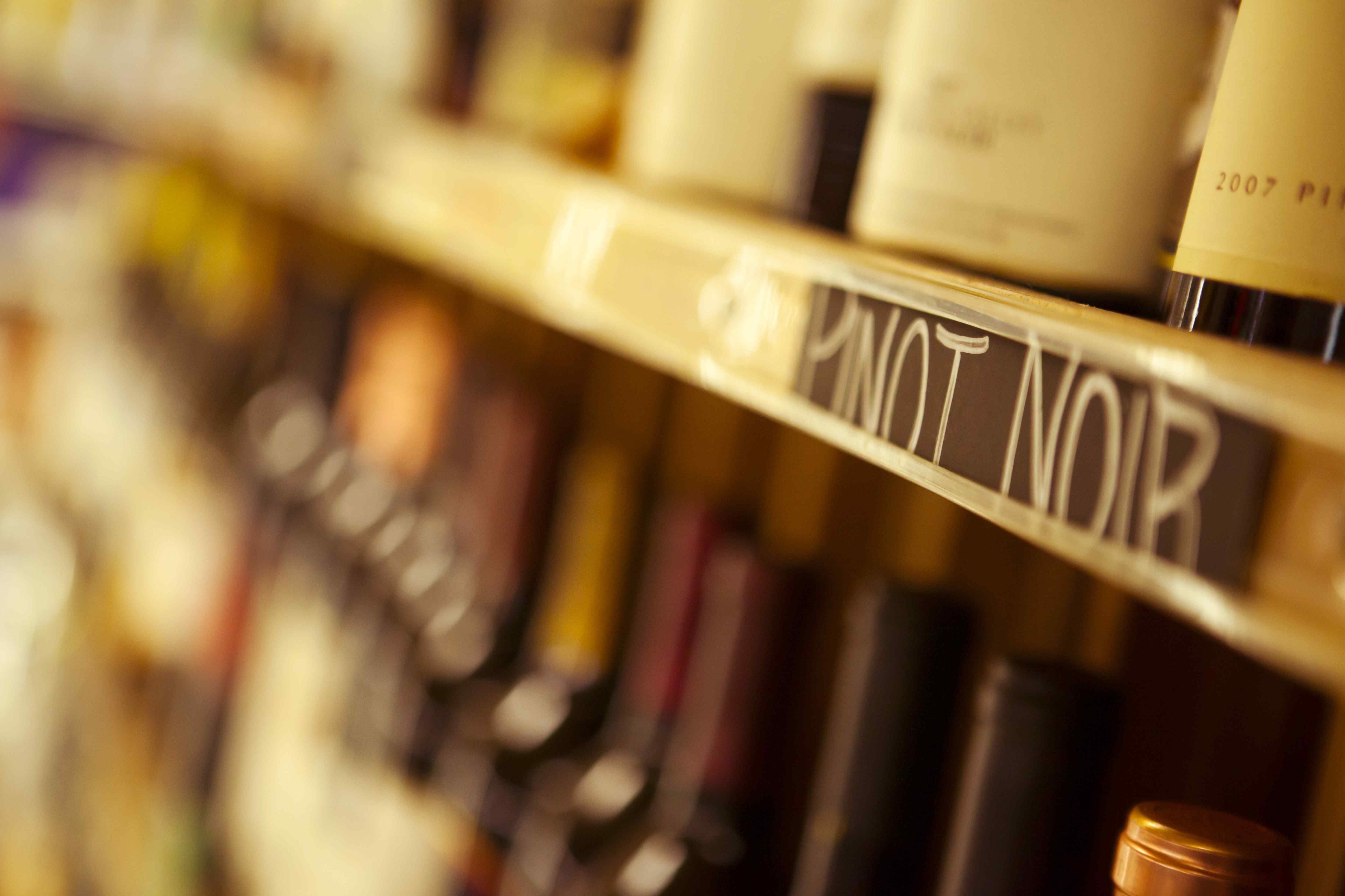 Close-up of a wine rack shelf label reading Pinot Noir, with bottles blurred in the background.