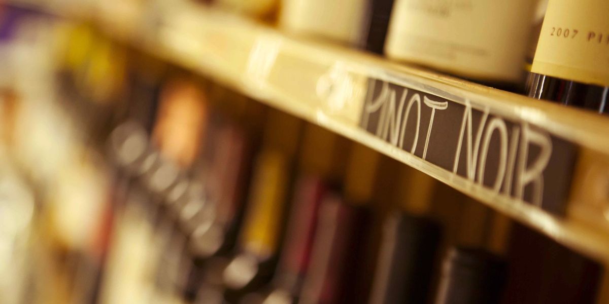 Close-up of a wine rack shelf label reading Pinot Noir, with bottles blurred in the background.