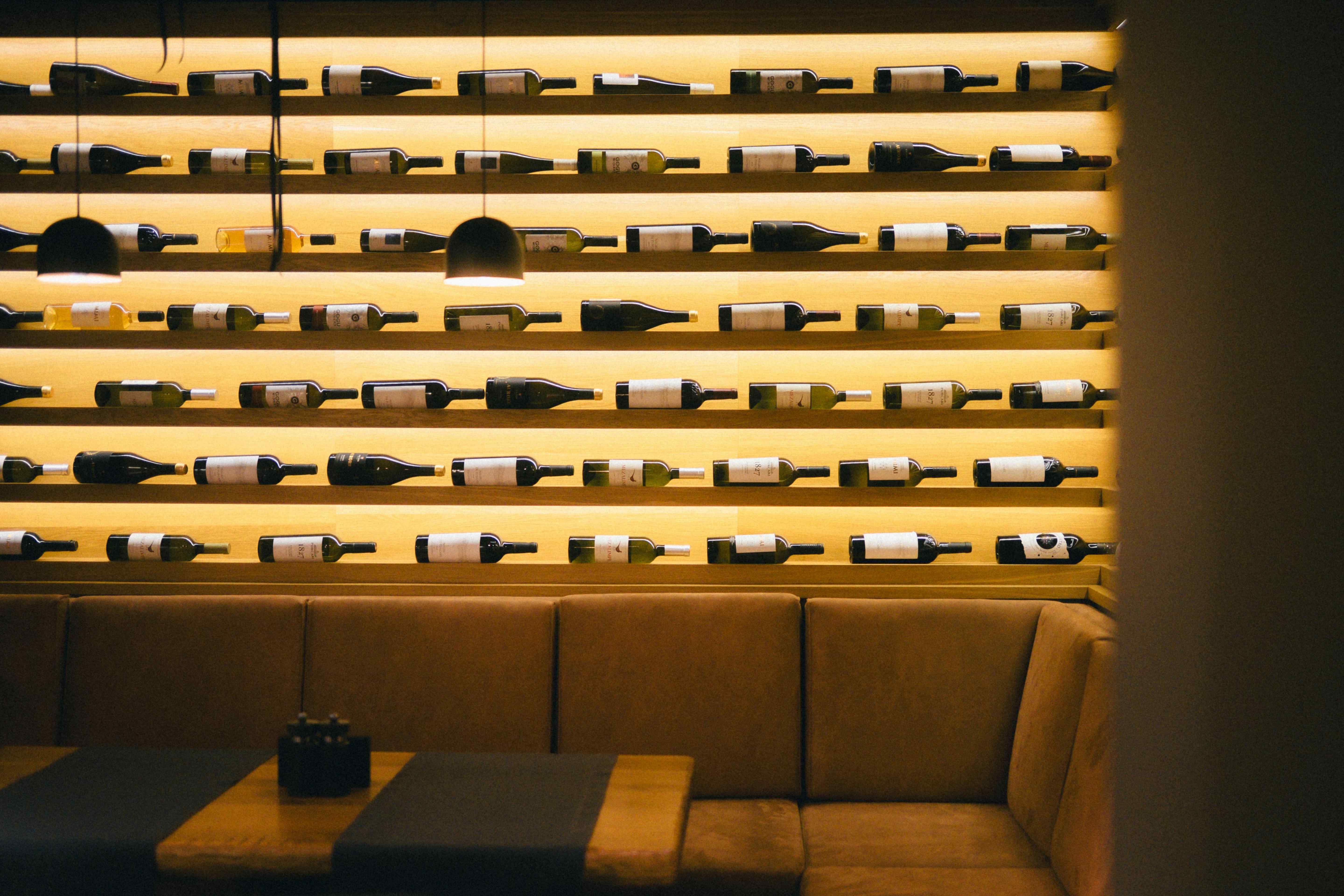 Backlit wine bottle shelving lining a restaurant wall above a leather booth seating area.