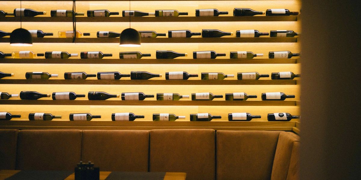 Backlit wine bottle shelving lining a restaurant wall above a leather booth seating area.