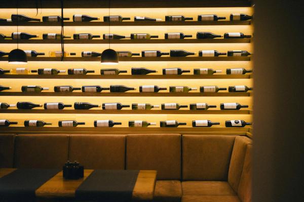 Backlit wine bottle shelving lining a restaurant wall above a leather booth seating area.