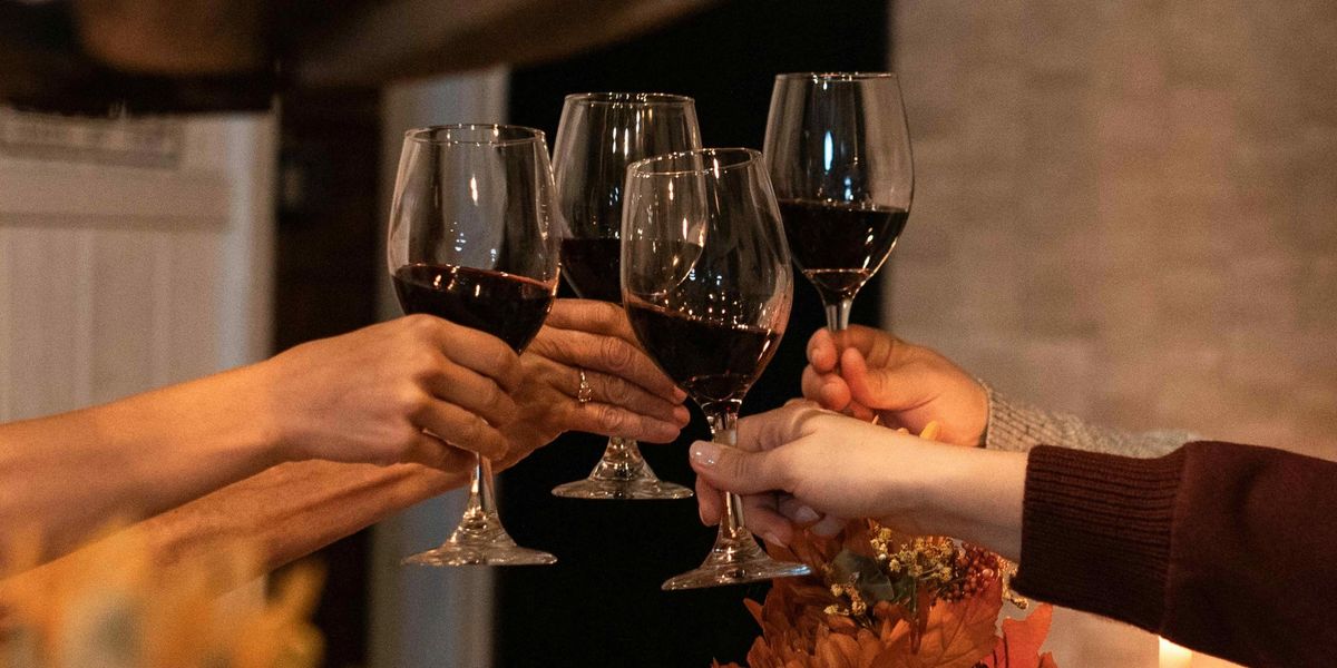 Four hands clinking glasses of red wine together near an autumn floral arrangement.