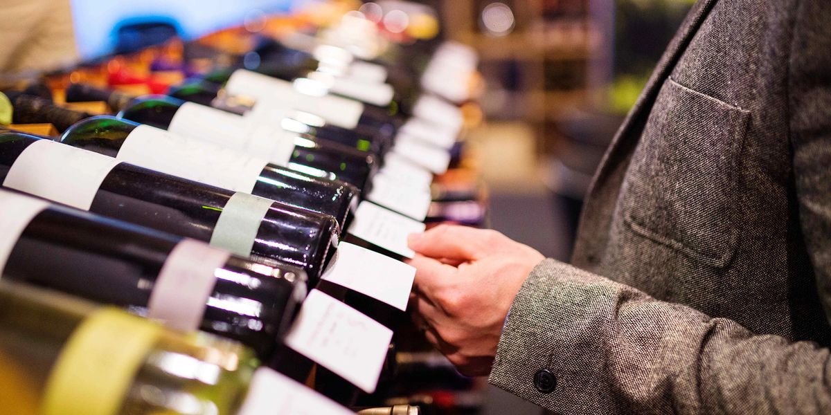 A collector browsing wine bottles on a shop shelf, checking labels before purchasing.