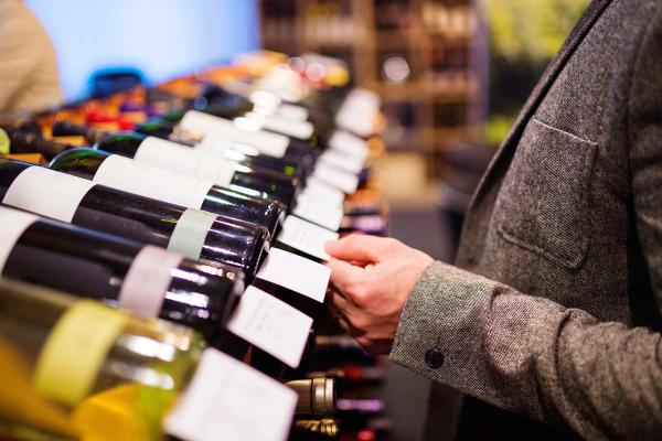 A collector browsing wine bottles on a shop shelf, checking labels before purchasing.