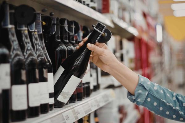 A red wine bottle being selected off the shelf at a wine shop.