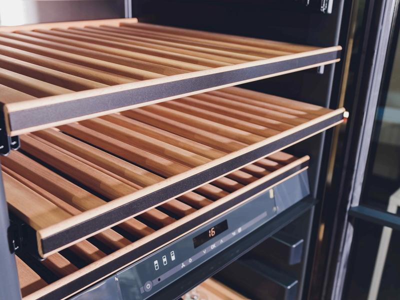 Open wine fridge shelf with wooden slats and a digital control panel displaying 16 degrees.
