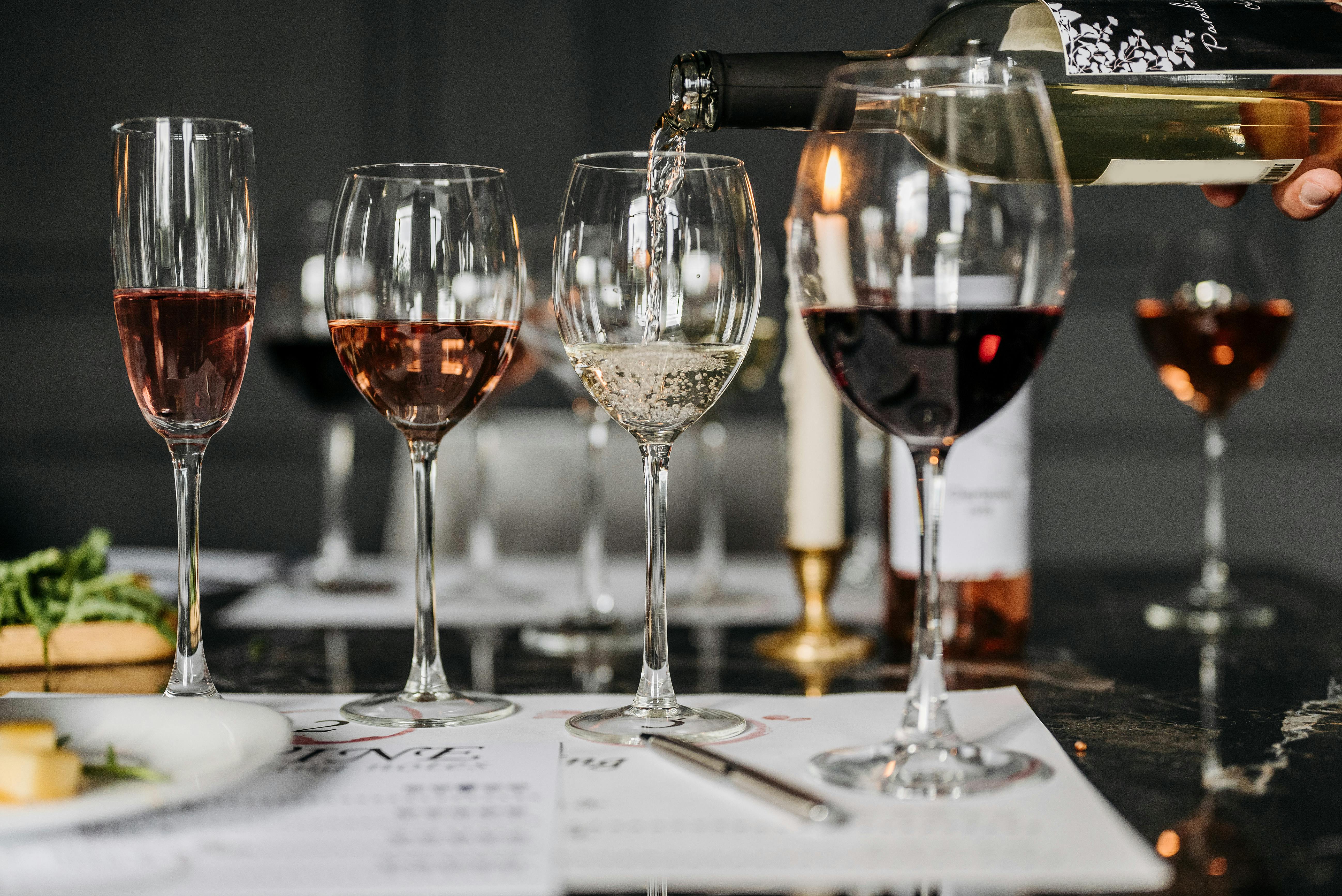 White wine pouring into a wine glass on a table, with other wine glasses full of different wine surrounding it.