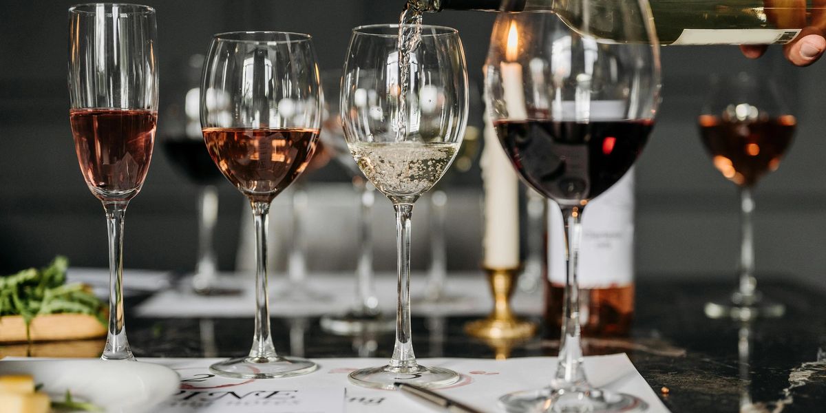 White wine pouring into a wine glass on a table, with other wine glasses full of different wine surrounding it.