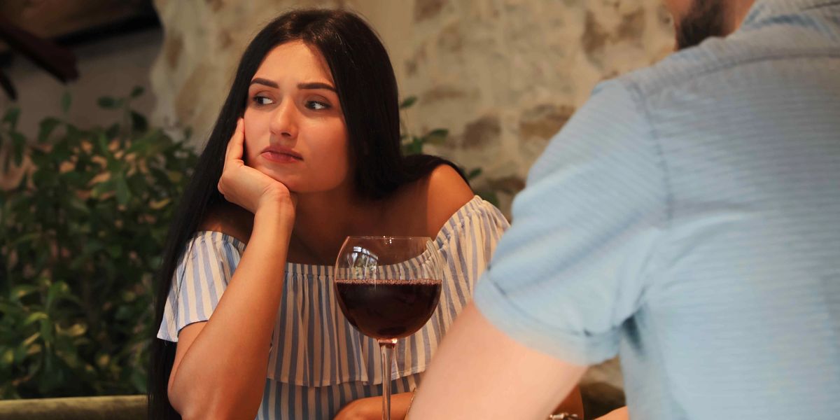Woman looking skeptically at a glass of red wine across a table from a man.