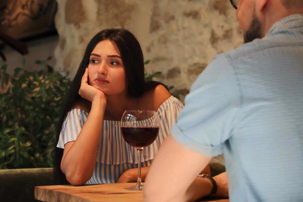 Woman looking skeptically at a glass of red wine across a table from a man.