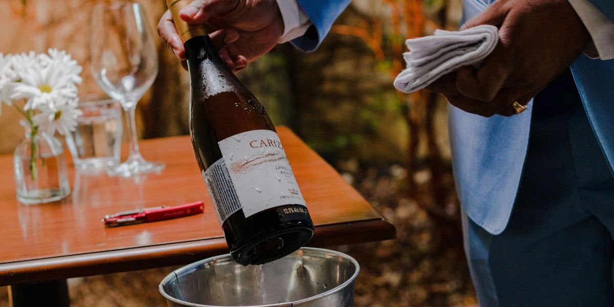 Server pouring a chilled white wine into an ice bucket at an outdoor table setting.