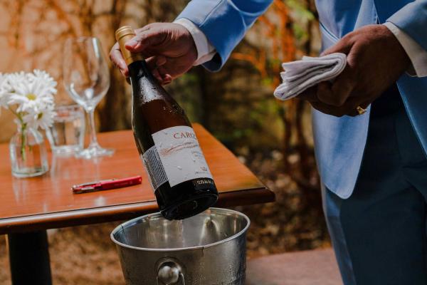 Server pouring a chilled white wine into an ice bucket at an outdoor table setting.