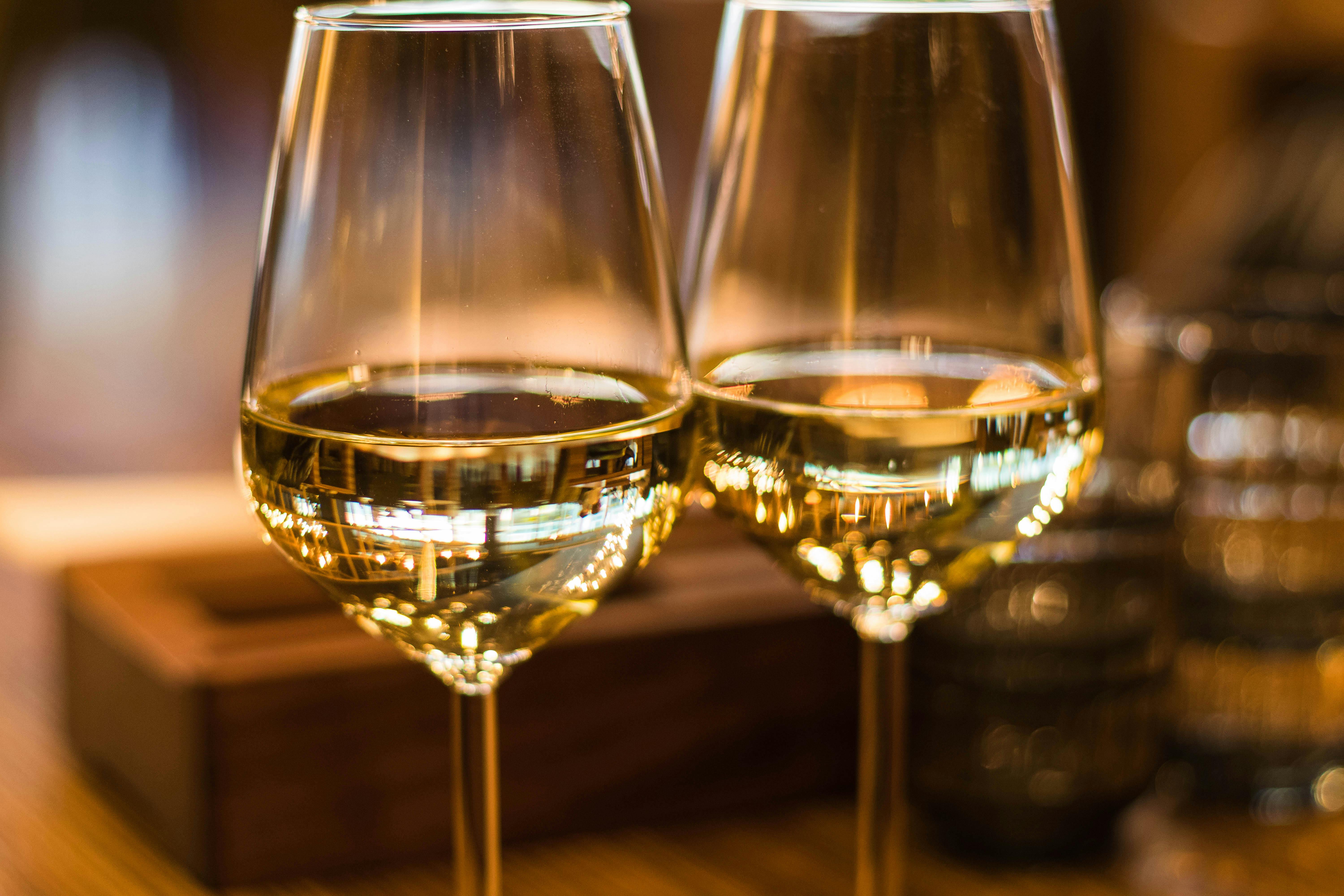 Two full glasses of white wine rest on a table in a warm, romantic restaurant setting.