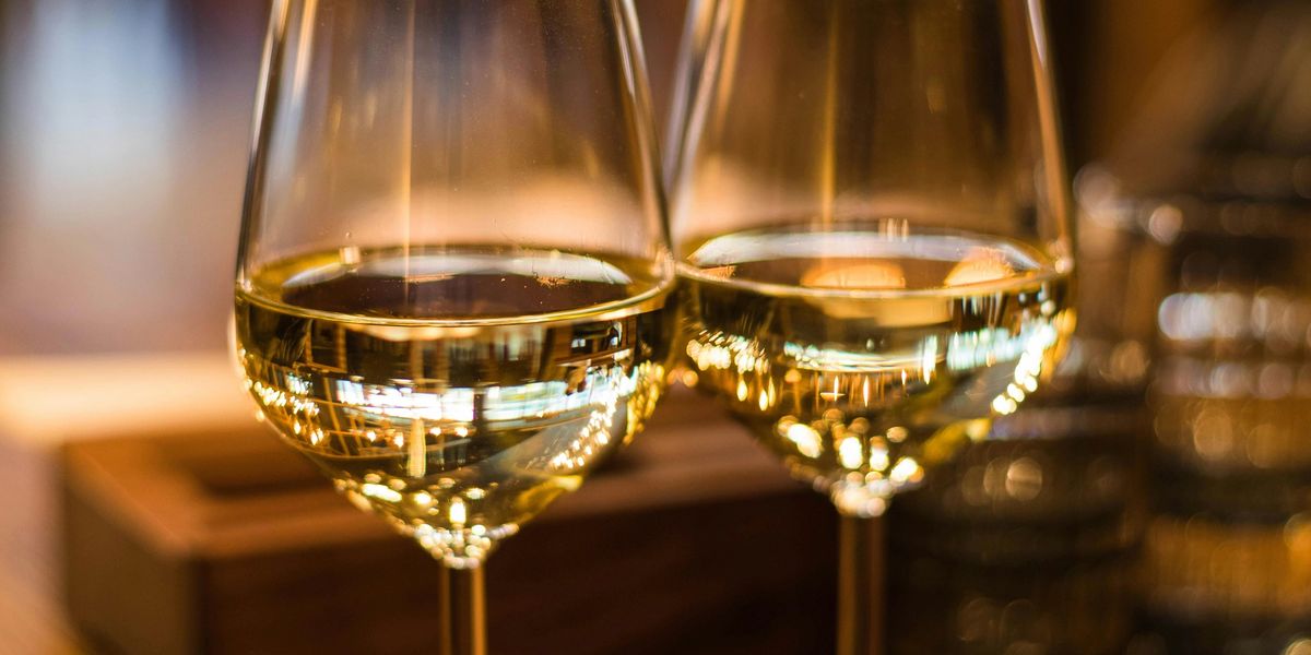 Two full glasses of white wine rest on a table in a warm, romantic restaurant setting.