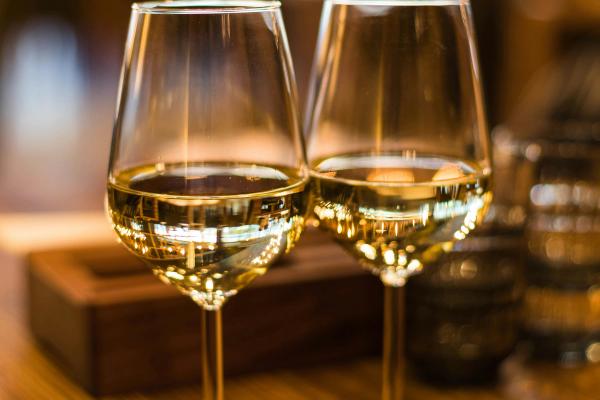 Two full glasses of white wine rest on a table in a warm, romantic restaurant setting.