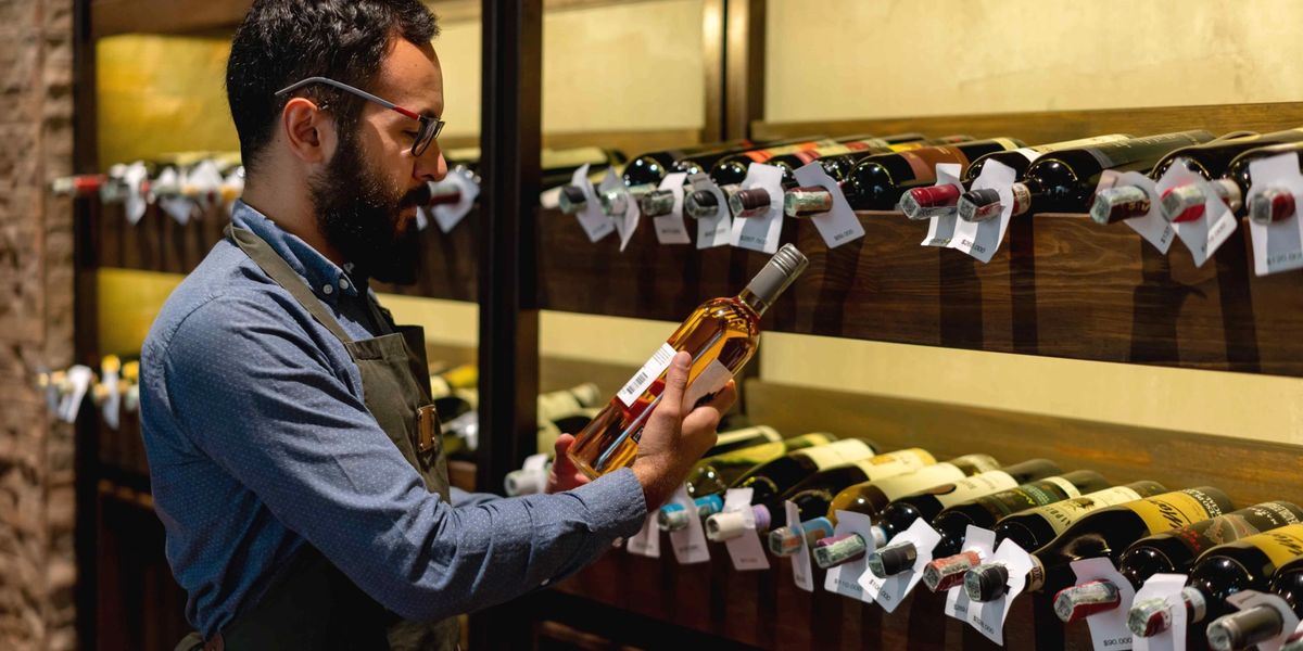 A sommelier analyzing the label of a wine bottle in a restaurant's wine cellar.