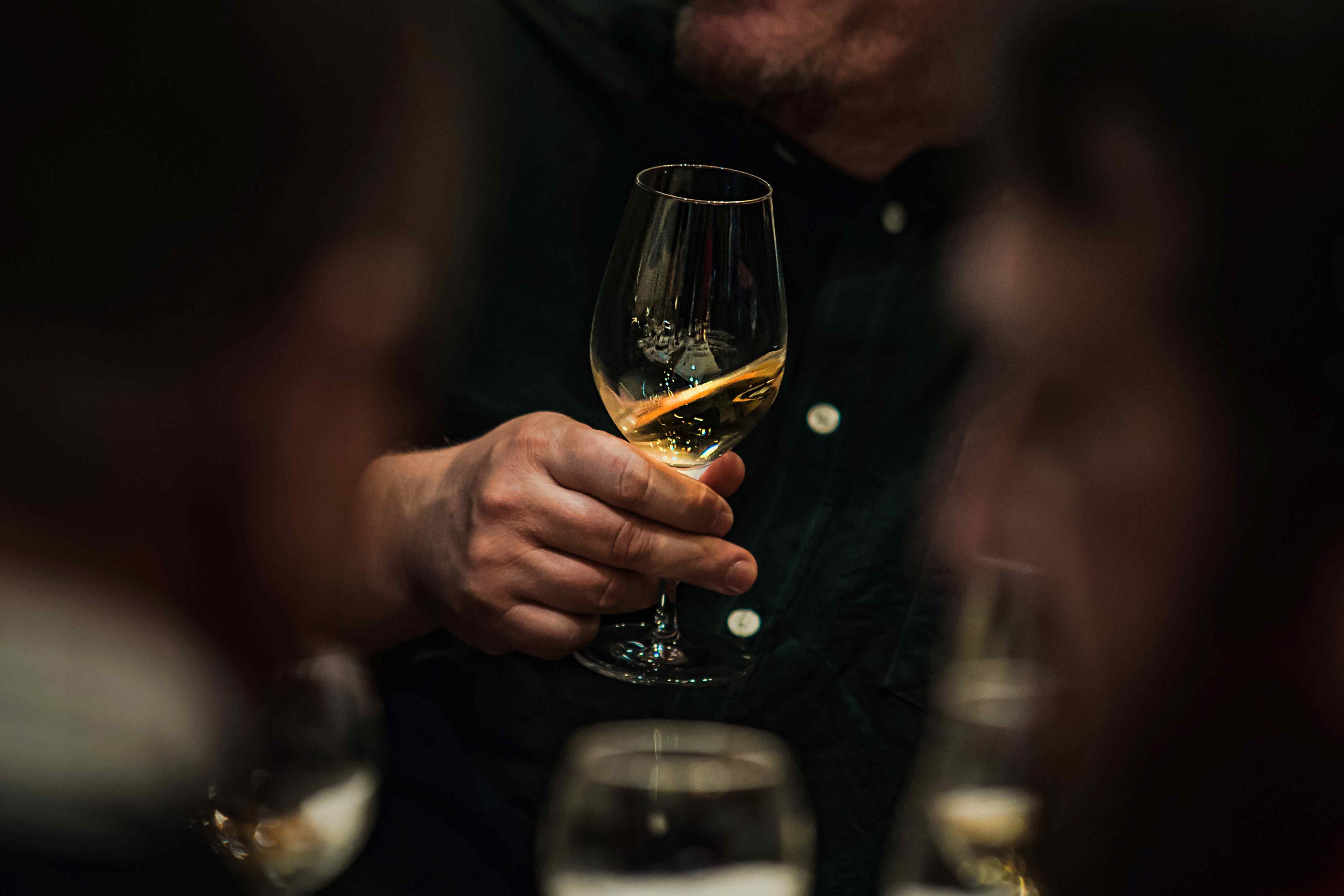 A man holding a glass of white wine at a dimly lit dinner table.