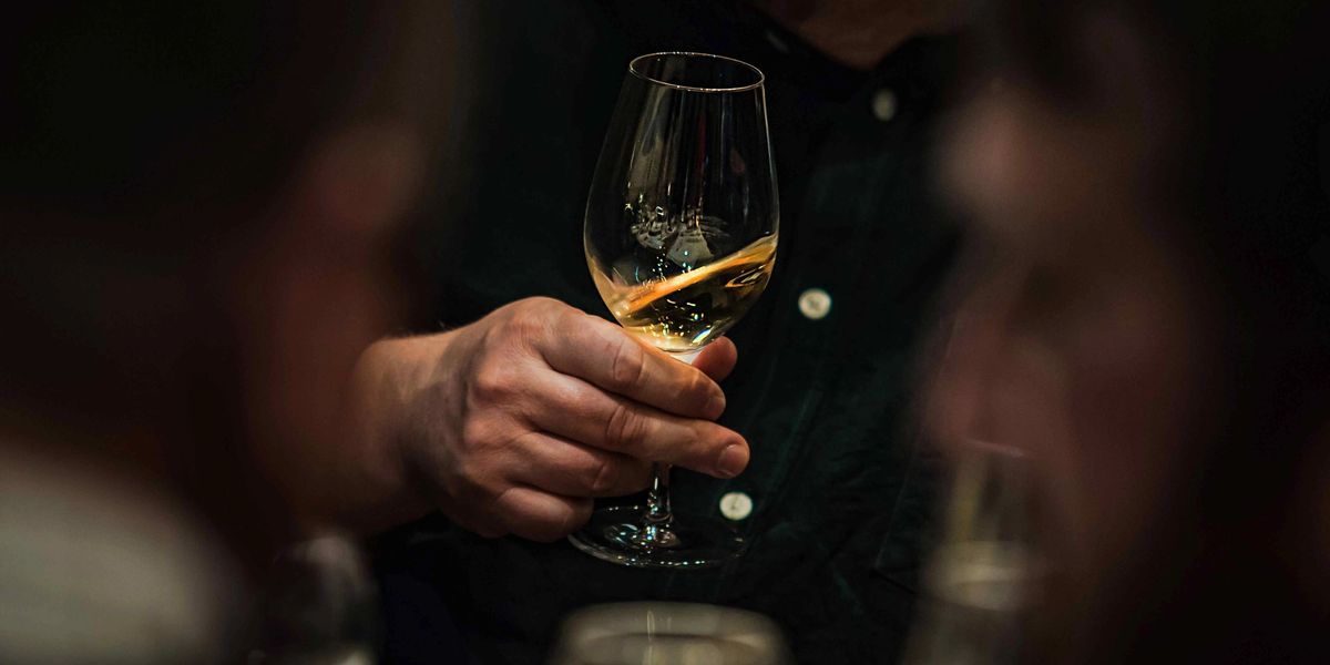 A man holding a glass of white wine at a dimly lit dinner table.