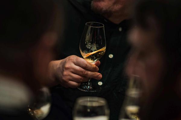 A man holding a glass of white wine at a dimly lit dinner table.
