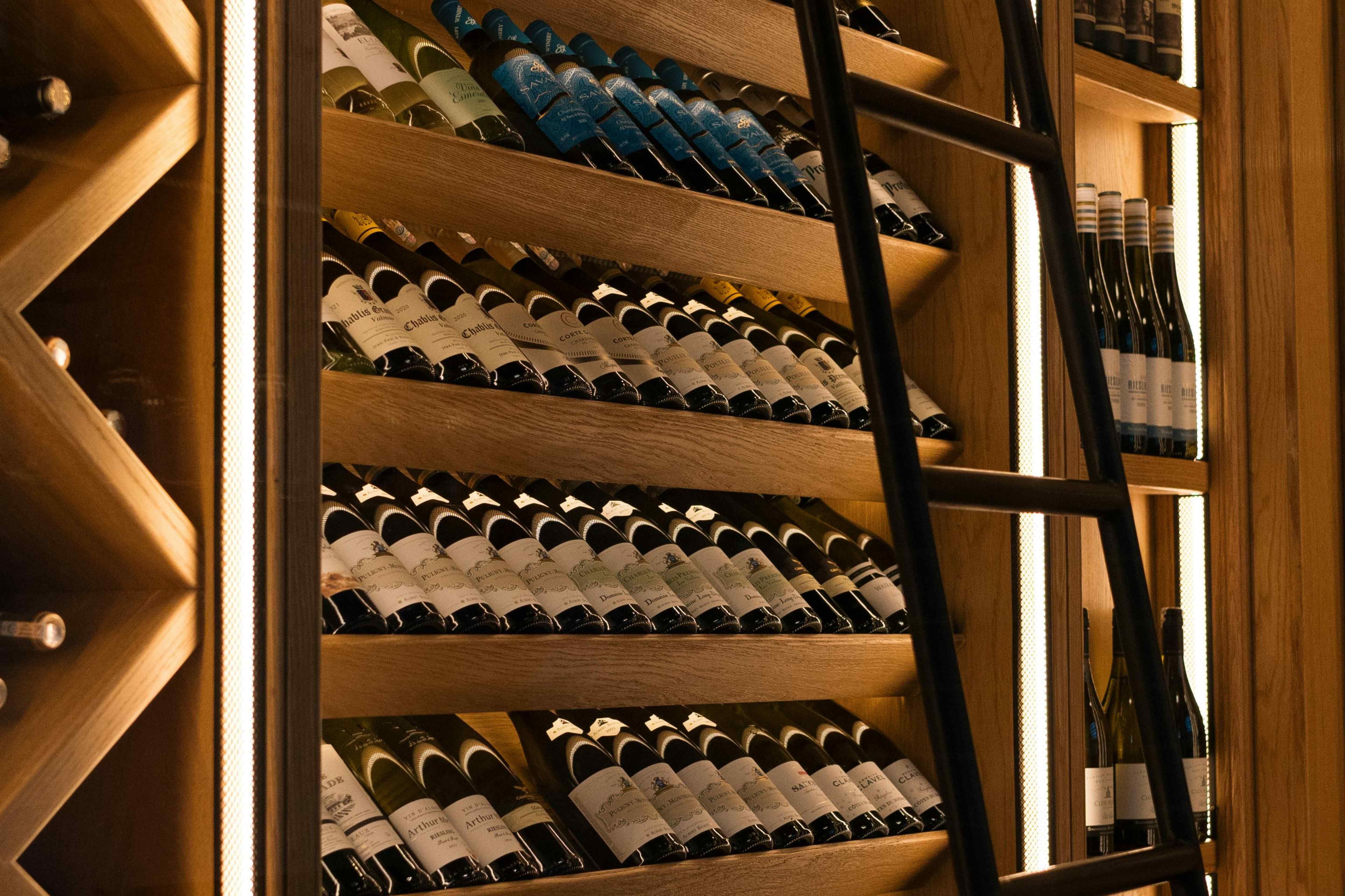 A large organized wine cellar with wooden shelves displaying hundreds of label-forward bottles and a rolling ladder.