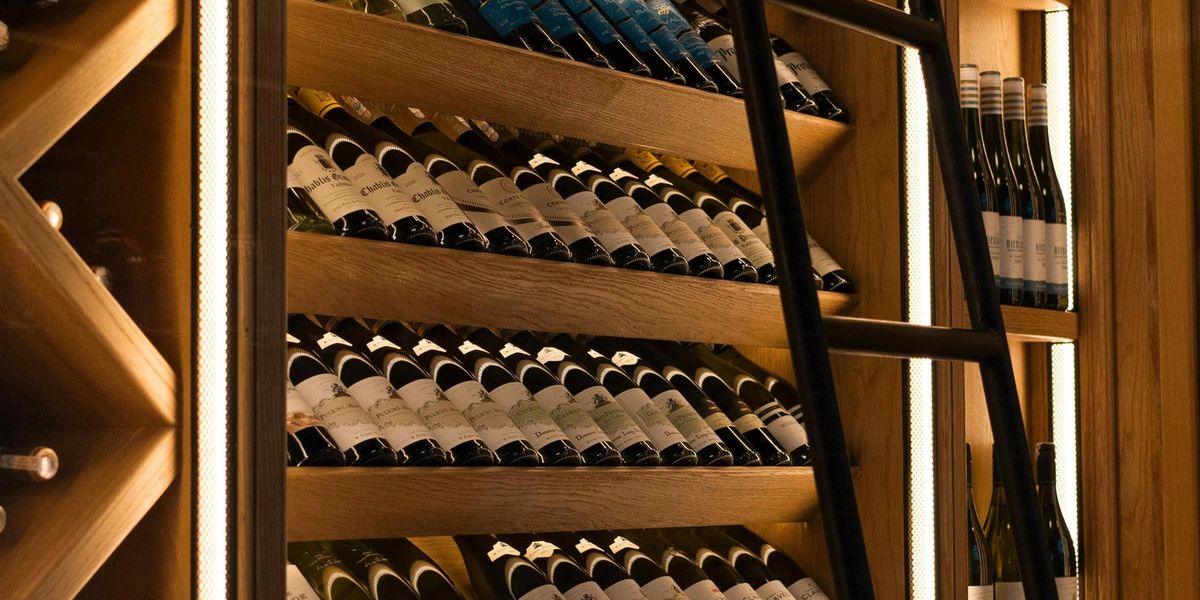 A large organized wine cellar with wooden shelves displaying hundreds of label-forward bottles and a rolling ladder.