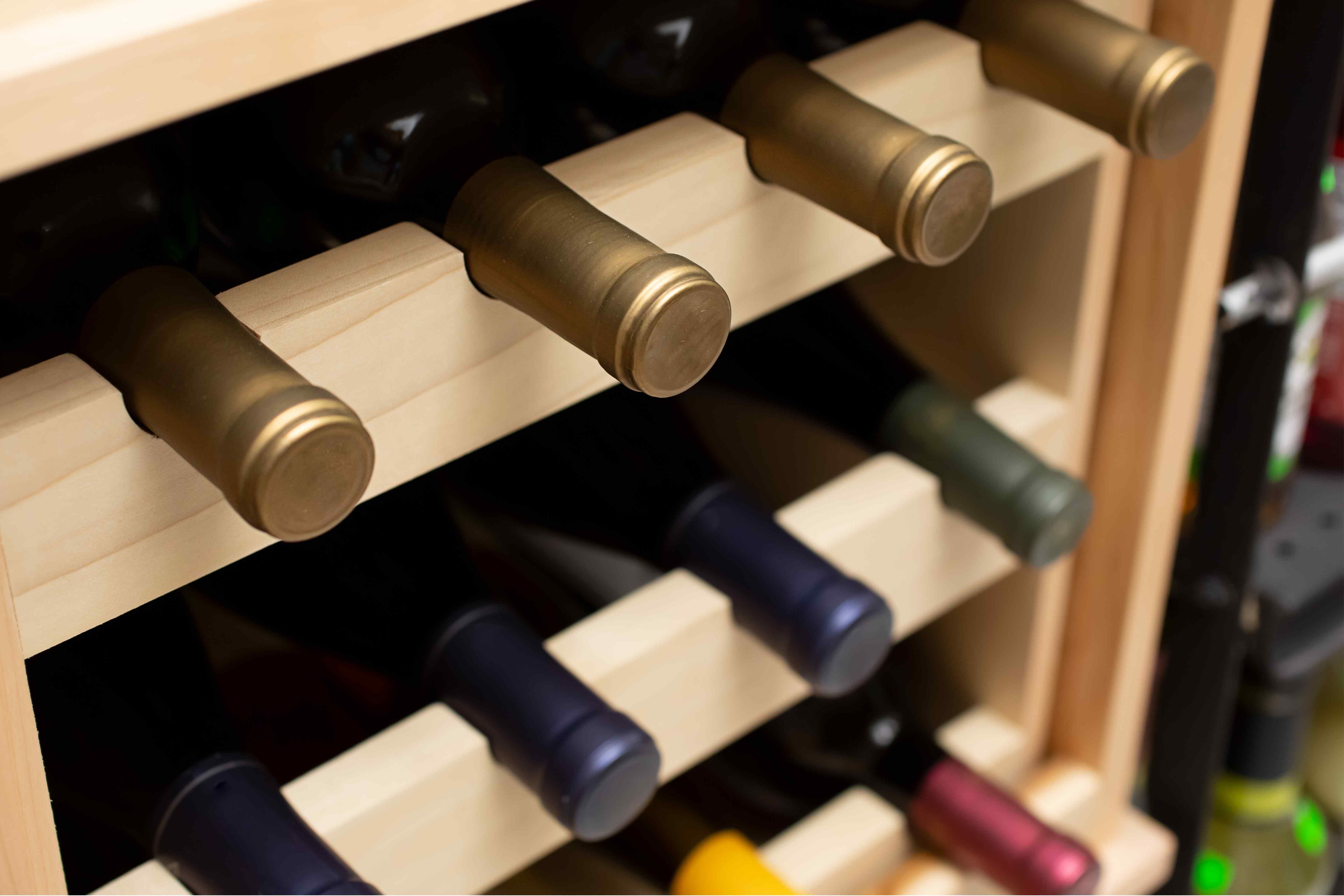 Wine bottles with gold, navy and burgundy foil capsules resting in a light wood rack.