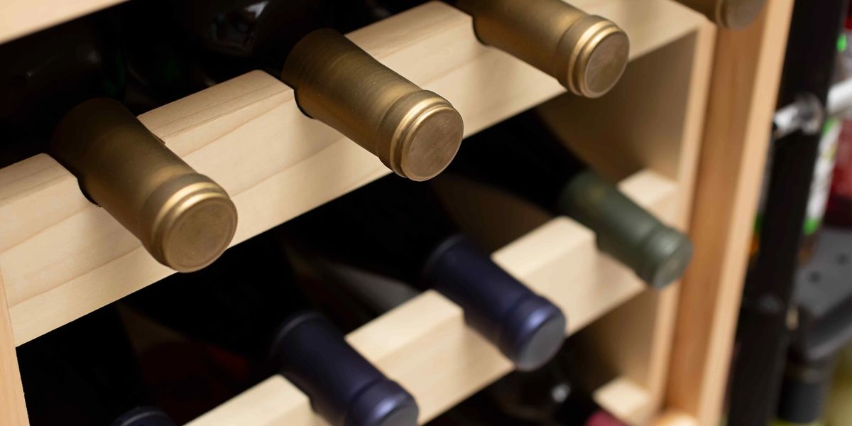 Wine bottles with gold, navy and burgundy foil capsules resting in a light wood rack.