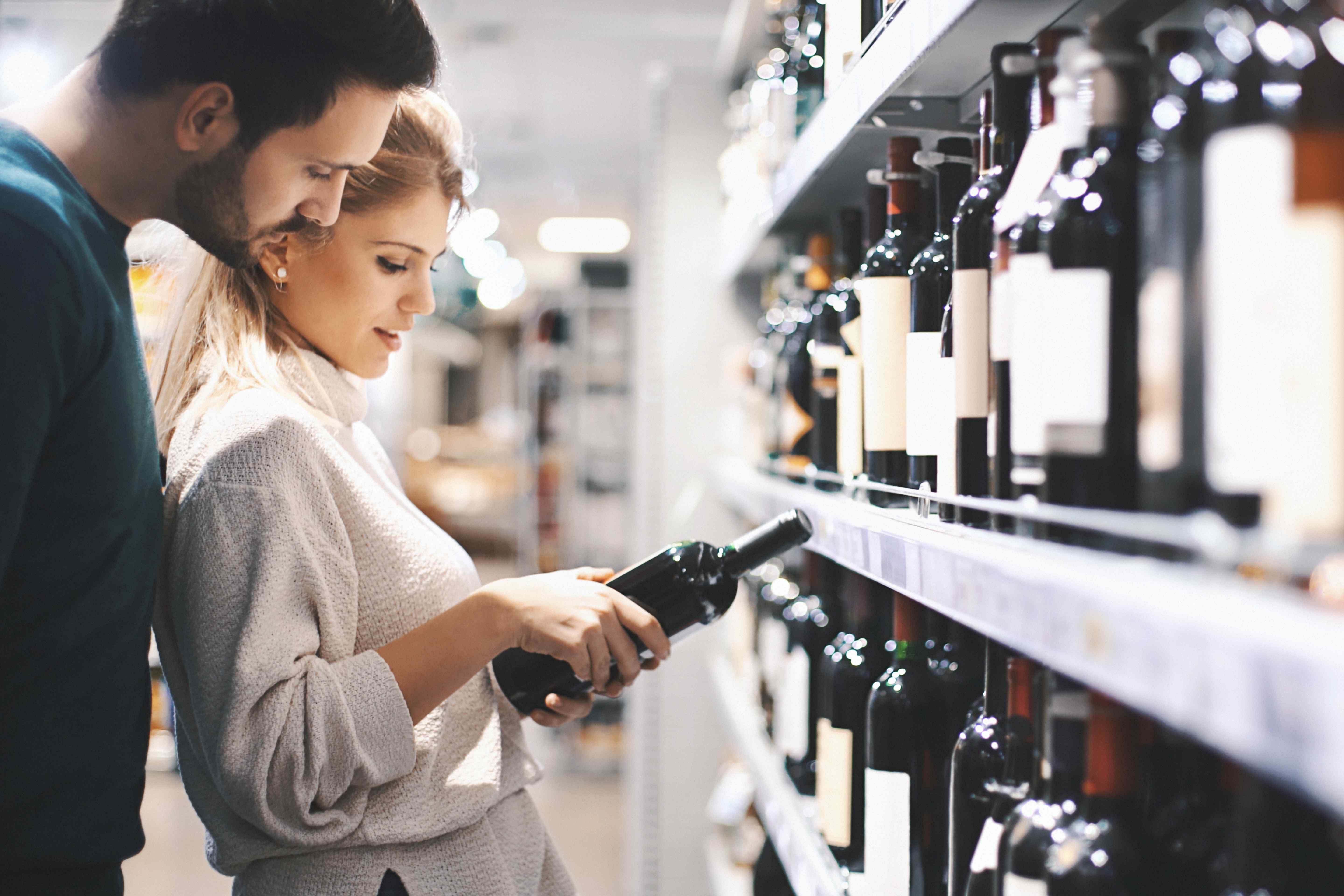 A couple reading a wine label together while shopping in a wine store.
