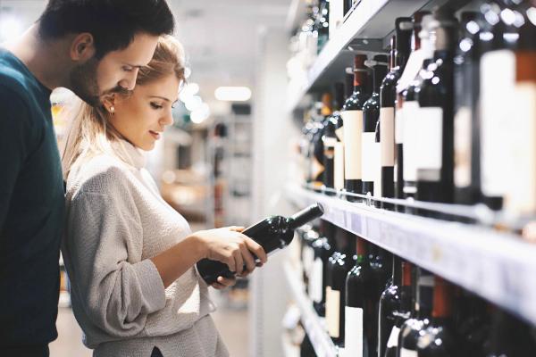 A couple reading a wine label together while shopping in a wine store.