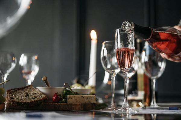 Sparkling rosé wine is poured into a Champagne flute on a table with bread, appetizers, and candles.
