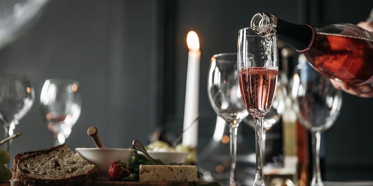 Sparkling rosé wine is poured into a Champagne flute on a table with bread, appetizers, and candles.