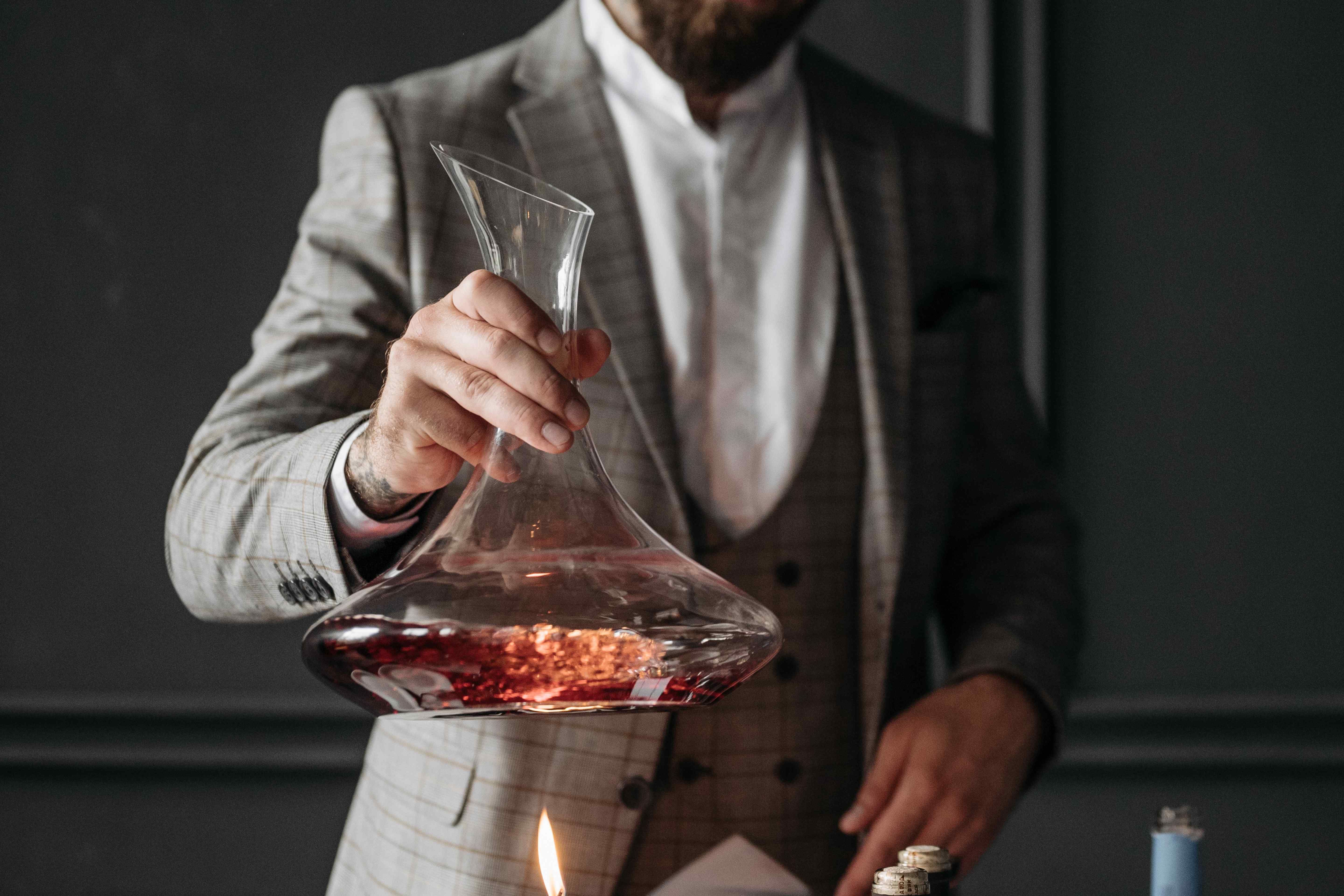 Man in a suit pouring red wine into a decanter over a lit candle to watch for sediment.