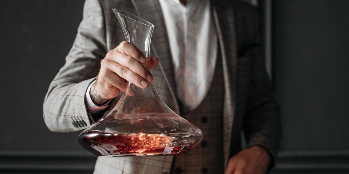Man in a suit pouring red wine into a decanter over a lit candle to watch for sediment.