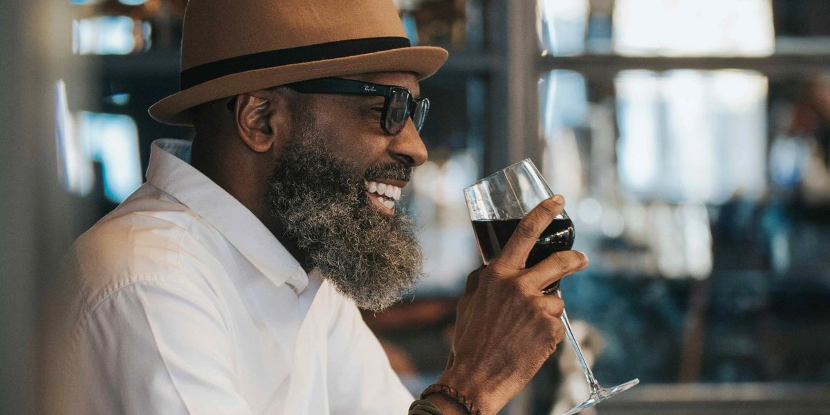A man smiling while holding a glass of red wine at a restaurant bar.